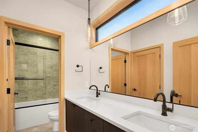bathroom featuring double vanity, a sink, enclosed tub / shower combo, and toilet