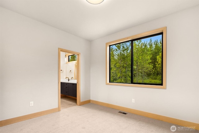 spare room featuring baseboards, visible vents, light carpet, and a sink