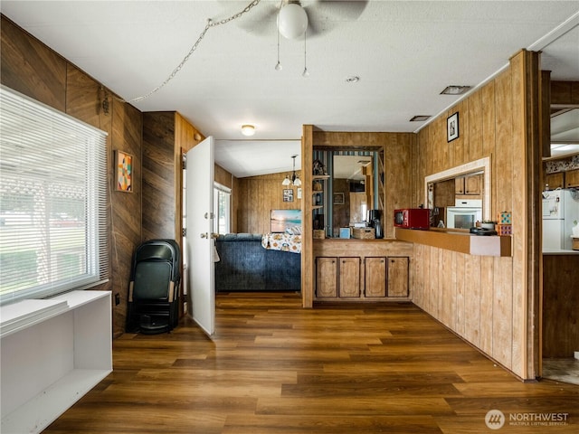 kitchen featuring brown cabinetry, wood finished floors, white appliances, ceiling fan, and wooden walls