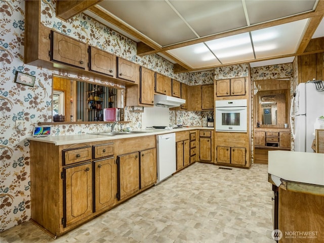 kitchen featuring white appliances, brown cabinets, wallpapered walls, and light countertops