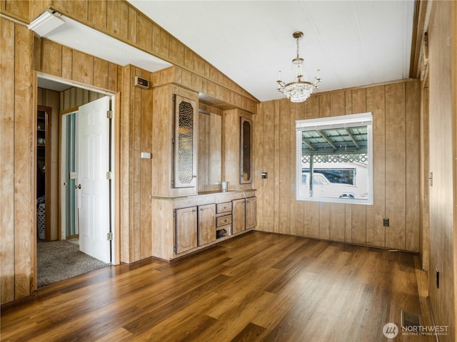 unfurnished dining area with visible vents, lofted ceiling, wooden walls, dark wood-type flooring, and a notable chandelier