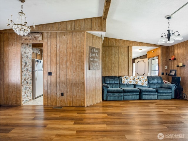 living area featuring wood walls, a notable chandelier, and vaulted ceiling