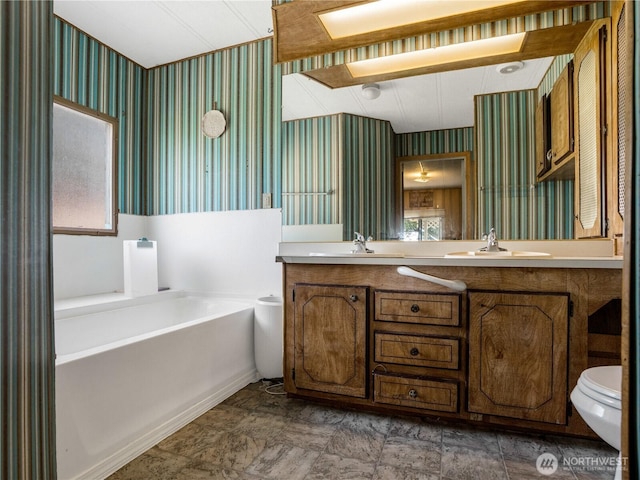 full bath with a sink, a bath, toilet, and wallpapered walls