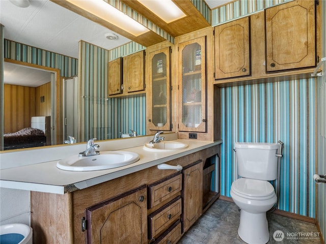 bathroom featuring a sink, toilet, and wallpapered walls