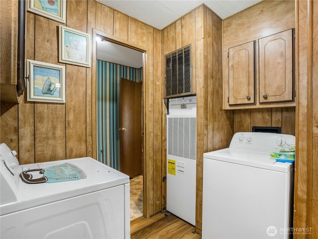 clothes washing area featuring a heating unit, washer and dryer, wooden walls, cabinet space, and light wood finished floors