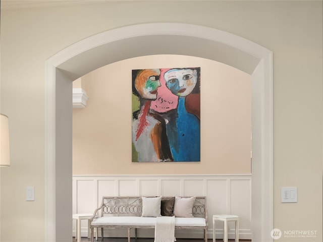 sitting room featuring arched walkways, wainscoting, and a decorative wall