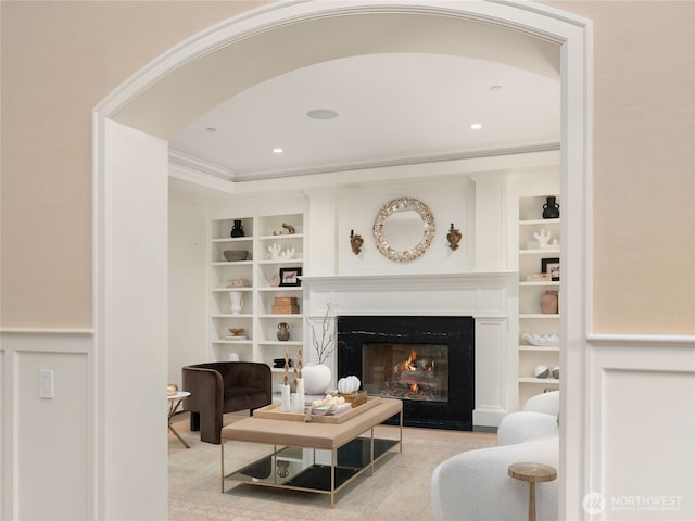 living room featuring arched walkways, a glass covered fireplace, built in shelves, and ornamental molding