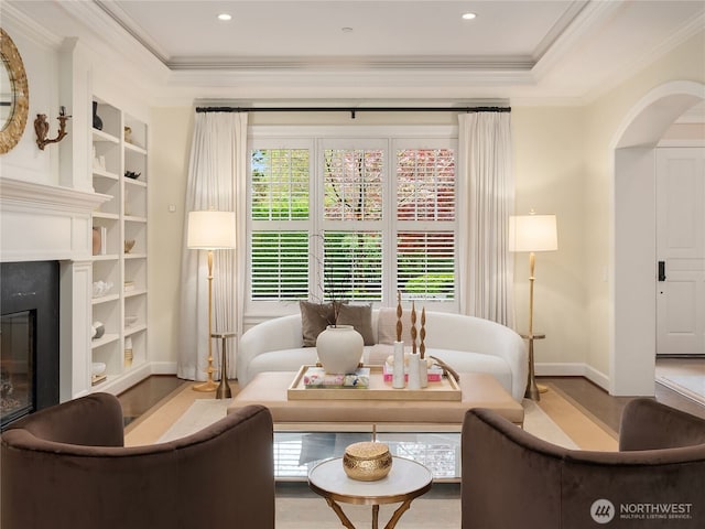 living area featuring arched walkways, wood finished floors, baseboards, ornamental molding, and a premium fireplace