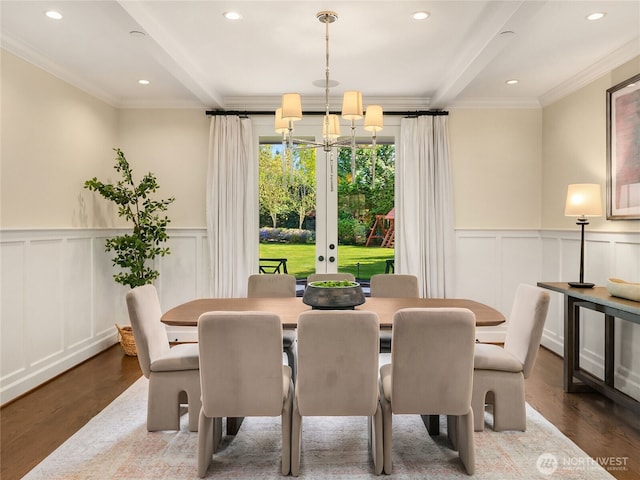 dining room with a decorative wall, a chandelier, wood finished floors, beamed ceiling, and ornamental molding