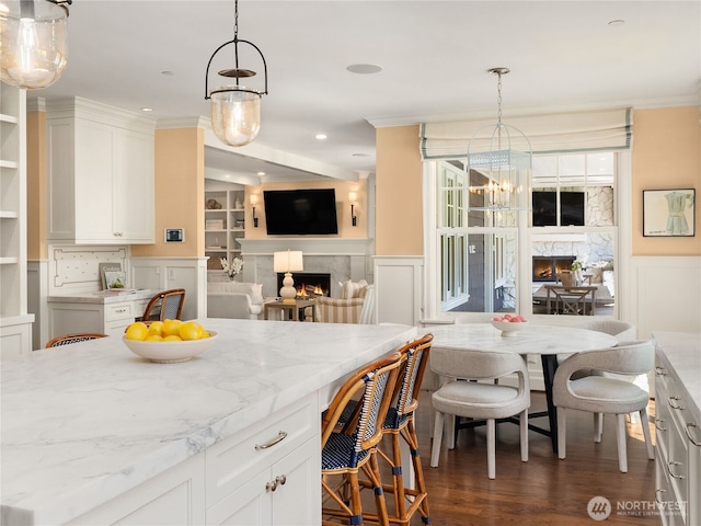 kitchen with a decorative wall, white cabinets, light stone counters, and a high end fireplace