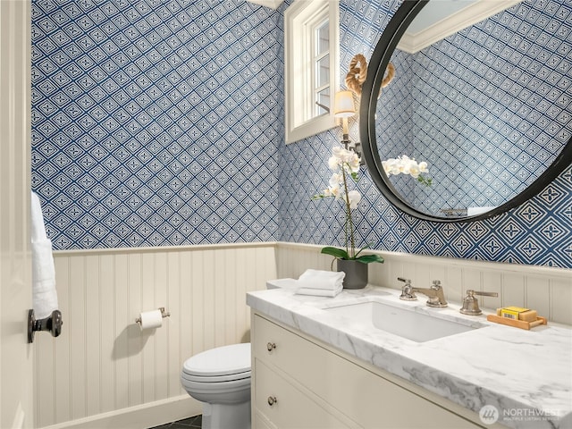 bathroom featuring toilet, wallpapered walls, wainscoting, and vanity
