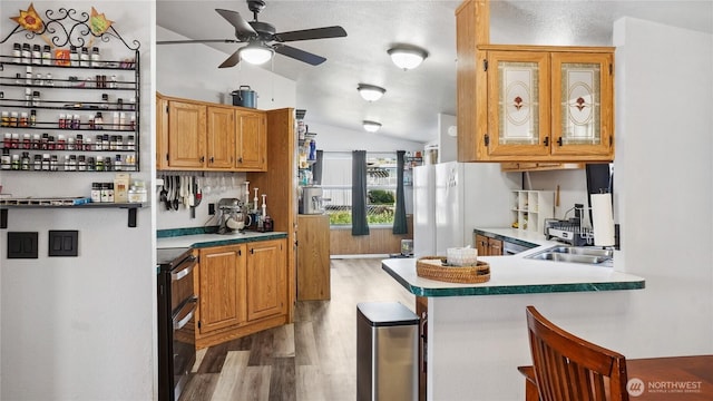 kitchen featuring wood finished floors, vaulted ceiling, freestanding refrigerator, ceiling fan, and a peninsula