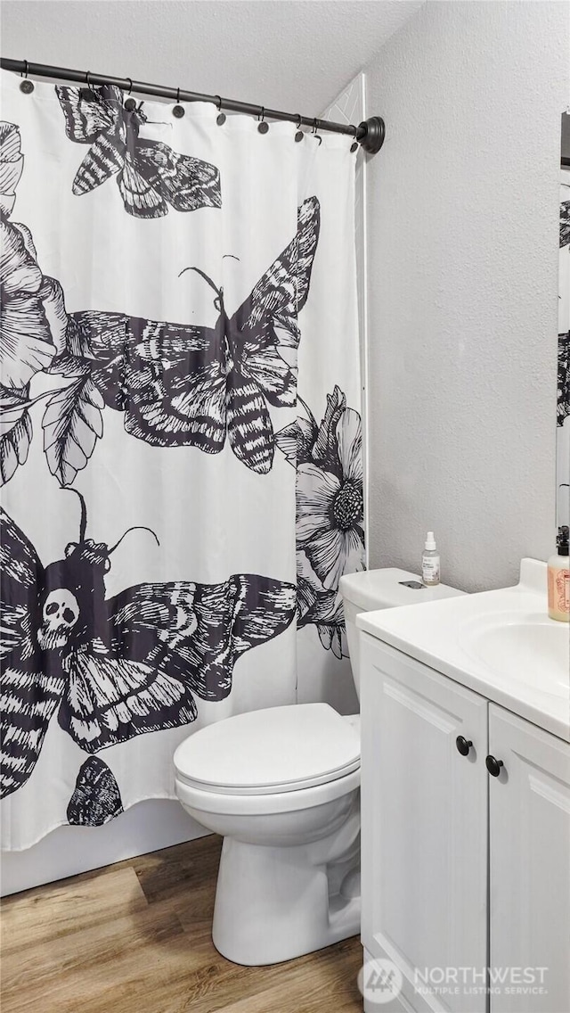 full bath with wood finished floors, toilet, a textured wall, vanity, and a shower with shower curtain