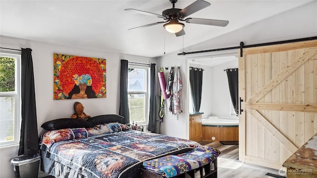 bedroom with light wood-style floors, a barn door, vaulted ceiling, and ceiling fan