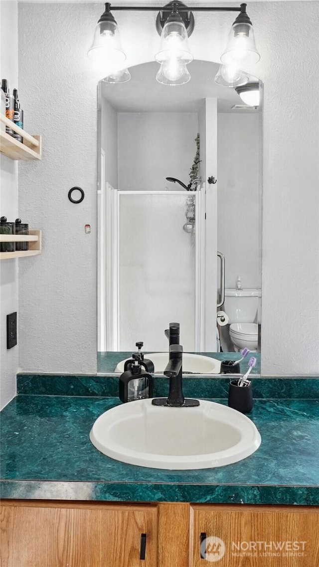 full bath featuring a shower stall, a textured wall, vanity, and toilet