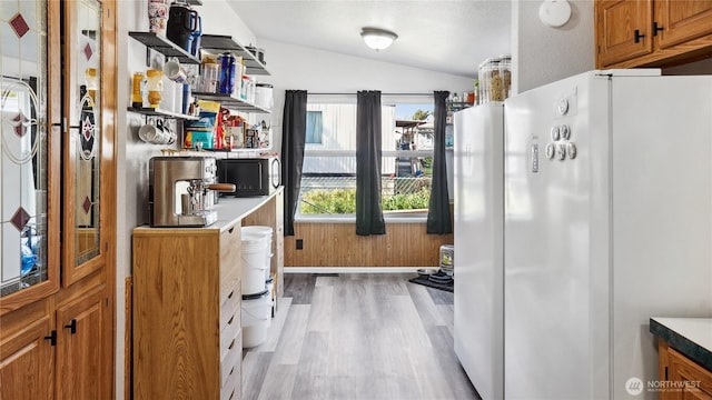 kitchen featuring freestanding refrigerator, vaulted ceiling, light wood-style flooring, black microwave, and brown cabinetry
