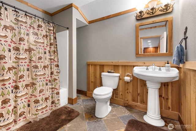 12430 Brooks St SW, Olympia, WA 98512 - bathroom with wooden walls, shower / tub combo with curtain, toilet, baseboards, and stone tile flooring