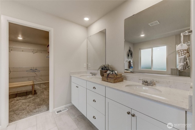bathroom with double vanity, a walk in closet, visible vents, and a sink