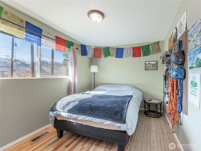 bedroom with baseboards, visible vents, and wood finished floors