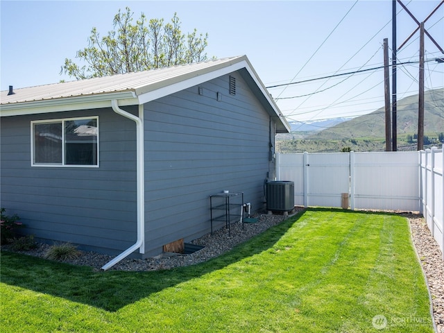 view of side of property featuring fence, central air condition unit, metal roof, a lawn, and a mountain view