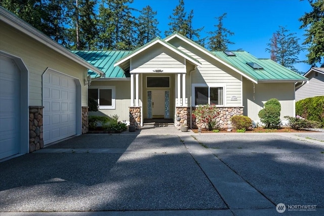 view of front of house featuring stone siding, a garage, a standing seam roof, driveway, and metal roof