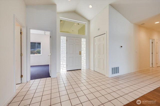 entryway featuring light tile patterned flooring, high vaulted ceiling, visible vents, and baseboards
