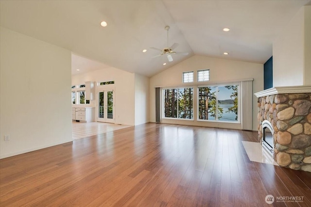 unfurnished living room with a ceiling fan, high vaulted ceiling, a stone fireplace, and wood finished floors