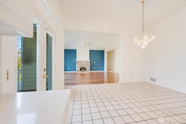 interior space with an inviting chandelier, a stone fireplace, and visible vents