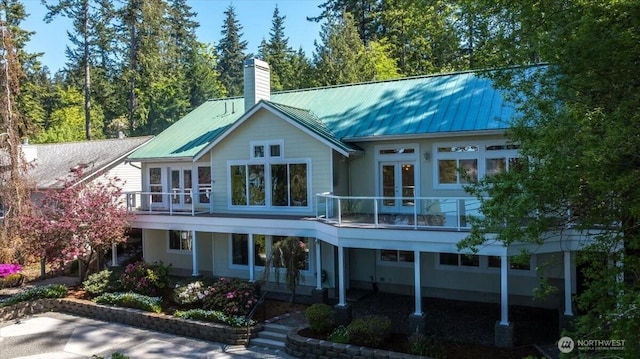 back of house with a balcony, french doors, a chimney, a standing seam roof, and metal roof
