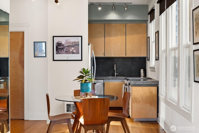 kitchen with light wood finished floors, backsplash, dark countertops, track lighting, and stainless steel dishwasher