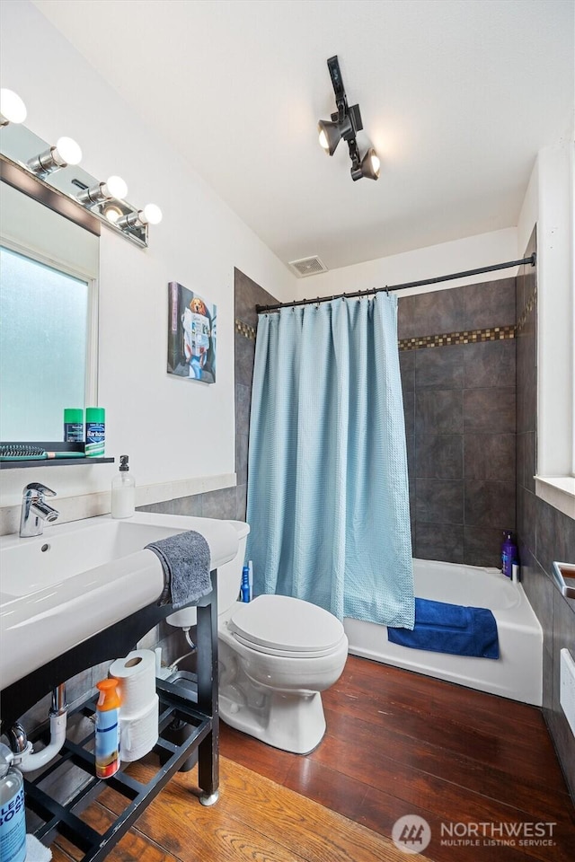 bathroom with toilet, shower / tub combo, visible vents, and wood finished floors