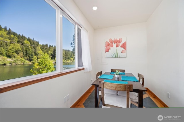 dining space with a water view, wood finished floors, baseboards, and recessed lighting