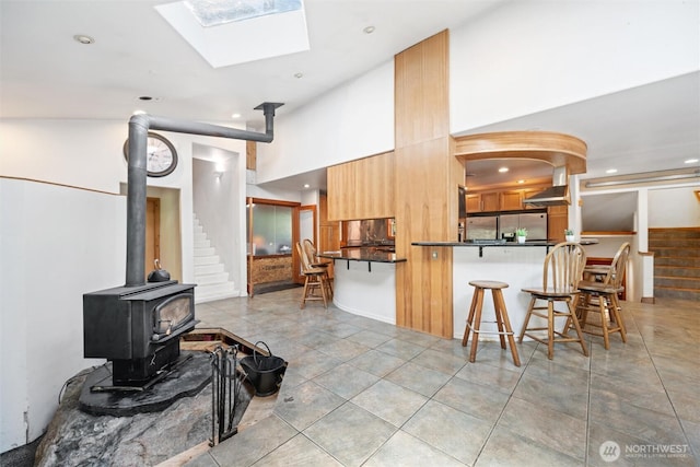kitchen with a breakfast bar area, dark countertops, stainless steel refrigerator with ice dispenser, a wood stove, and recessed lighting