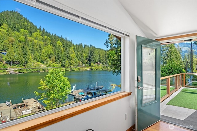 doorway with vaulted ceiling, a wooded view, a water view, and wood finished floors