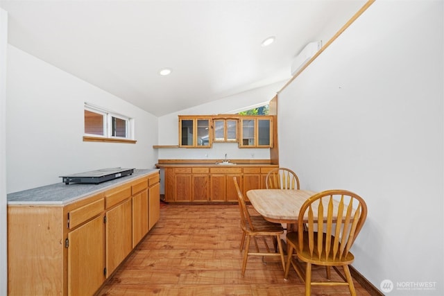 kitchen with a sink, light wood-type flooring, vaulted ceiling, light countertops, and glass insert cabinets