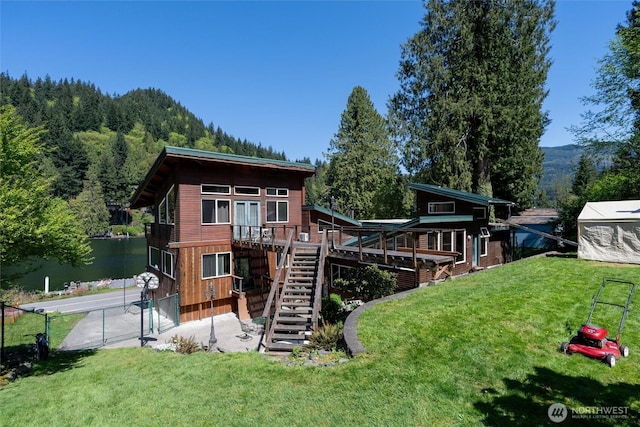 rear view of property with a yard, stairs, a deck with water view, and fence