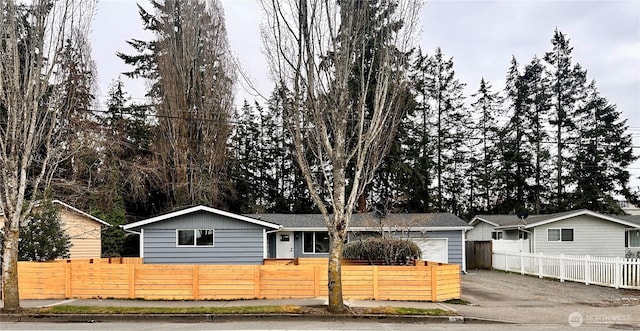 ranch-style house featuring a garage, a fenced front yard, and aphalt driveway