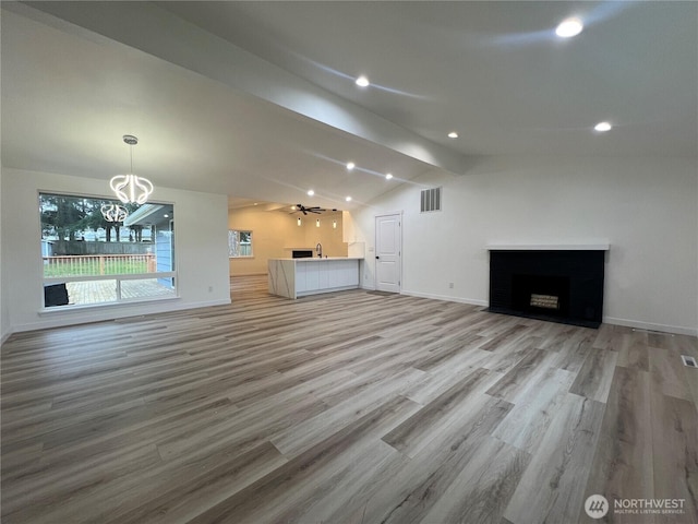 unfurnished living room featuring a notable chandelier, lofted ceiling with beams, a fireplace, light wood-style flooring, and visible vents
