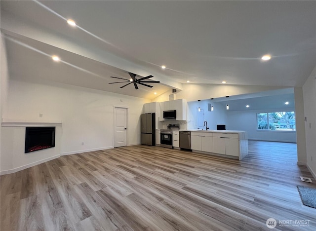 unfurnished living room with a sink, light wood-style floors, a fireplace, vaulted ceiling with beams, and visible vents
