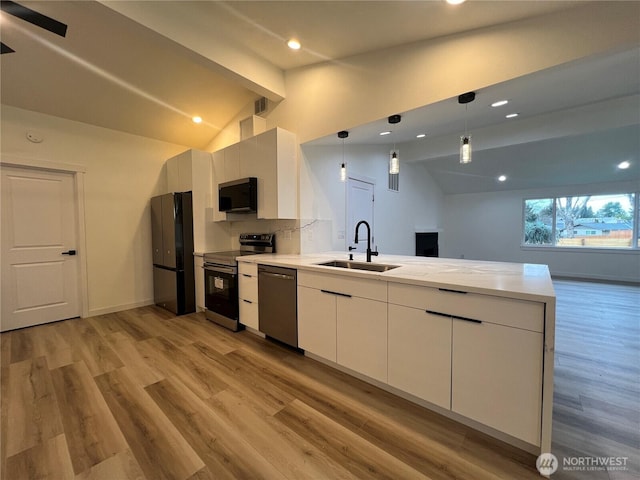 kitchen with appliances with stainless steel finishes, vaulted ceiling, a sink, light wood finished floors, and a peninsula
