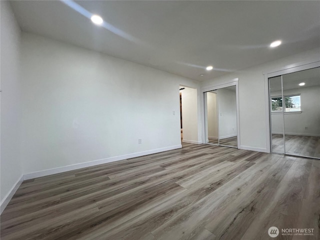 unfurnished bedroom with multiple closets, baseboards, recessed lighting, and wood finished floors