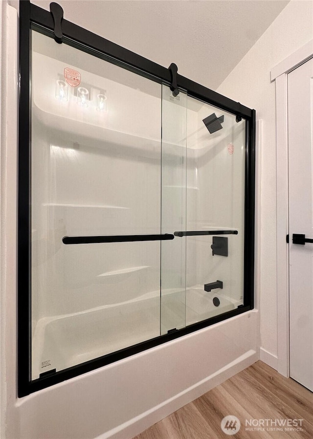 bathroom featuring baseboards, bath / shower combo with glass door, and wood finished floors