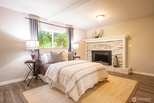 bedroom featuring baseboards, a fireplace with raised hearth, and wood finished floors