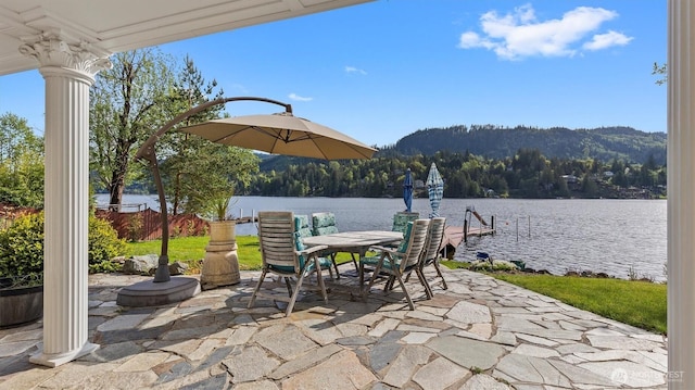 view of patio / terrace featuring a water and mountain view, outdoor dining space, a wooded view, and a dock