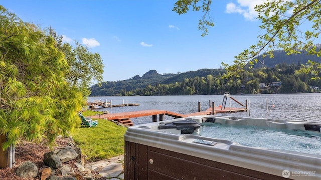 dock area with a hot tub, a view of trees, and a water and mountain view