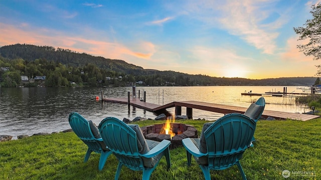 view of dock featuring a lawn, a water view, a fire pit, and a wooded view