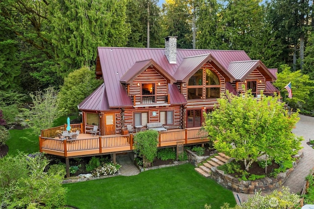 back of house with log exterior, a deck, a chimney, a lawn, and metal roof