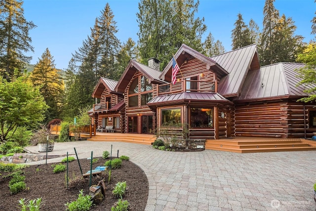 back of property with log exterior, a patio area, a balcony, a standing seam roof, and metal roof