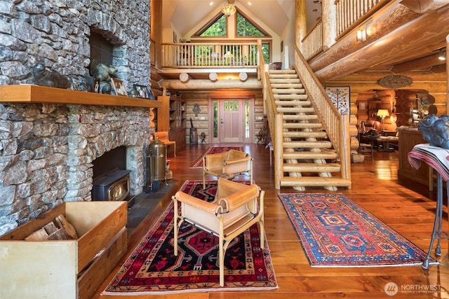 living area featuring wood-type flooring, a wood stove, log walls, stairs, and high vaulted ceiling
