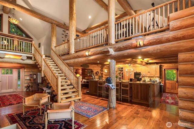 living area featuring stairway, high vaulted ceiling, rustic walls, beamed ceiling, and hardwood / wood-style floors